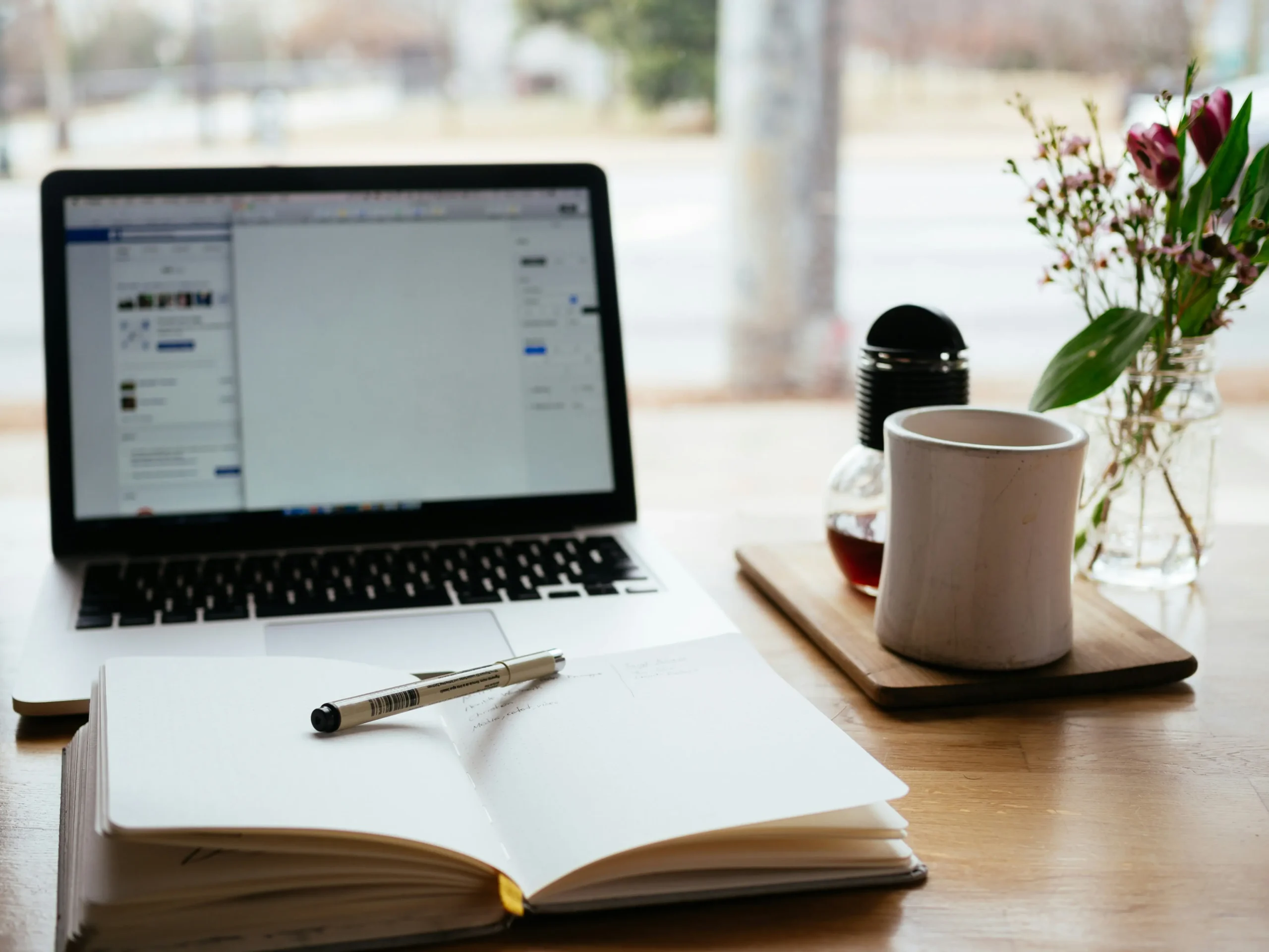 Open notebook with pen on top in front of laptop and a coffee mug